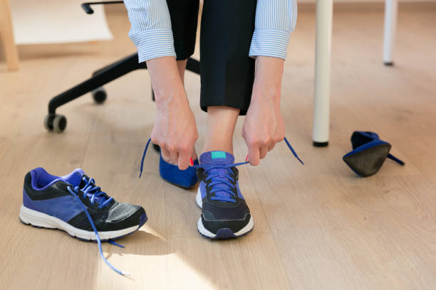 femme changeant des talons hauts, chaussures de bureau après jour de travail tout en s’asseyant sur la chaise, prêt à prendre une promenade ou courir - marché du travail photos et images de collection