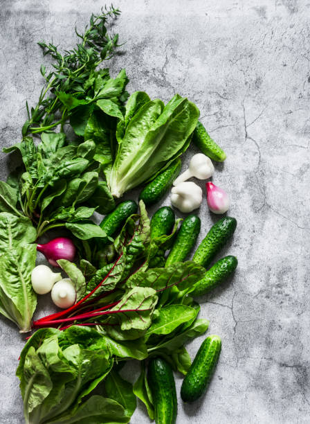 istock Fresh vegetables and herbs background. Cucumbers, romaine lettuce, chard, coriander, red onion, garlic, tarragon, lettuce, spinach on a gray background, top view. Copy space 1257331114