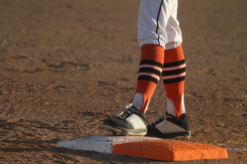 A close-up of the feet of a baseball player as he stands on first base in an image with room for copy on the left side of the frame.