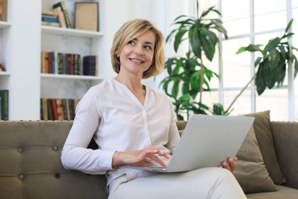 istock Cheerful middle aged woman using laptop while sitting on sofa at home. 1257337160