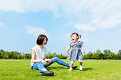 青空に対して緑の広場で遊ぶ母と小さな娘