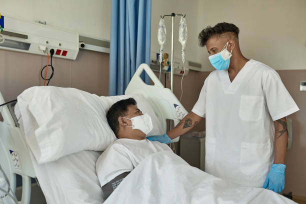 enfermera masculina apoyando la recuperación del paciente en la cama del hospital - filipino ethnicity asian ethnicity men male fotografías e imágenes de stock