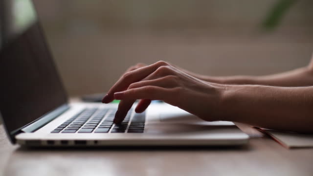 Close-up of hands of unrecognizable business person typing on laptop keyboard at desk in home office