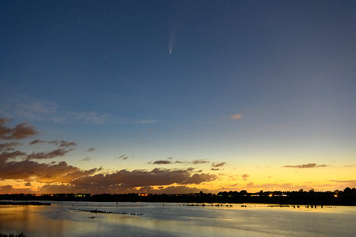 Comet Neowise in the dark night sky over The Reevediep lake and bridge near Kampen in Overijssel, The Netherlands on July 21, 2020. The comet is showing a trail.