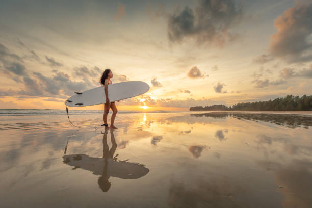 silhouette des surfens hawaiian surfer mädchen weibliche bikini frau blick auf ozean strand sonnenuntergang wasser stehen dateriert mit surfbrett. stolz auf sich selbst. bewölkten sonnenuntergang himmel tag. - activity asia atmosphere beach stock-fotos und bilder