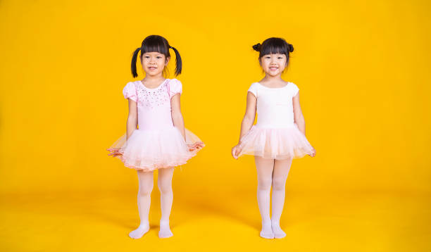 retrato de dos niñas asiáticas sueña con convertirse en bailarina en una falda de tutú rosa aislada sobre fondo amarillo. feliz jovencita practicando su baile. concepto de estilo de vida infantil de la infancia - ballet dress studio shot costume fotografías e imágenes de stock