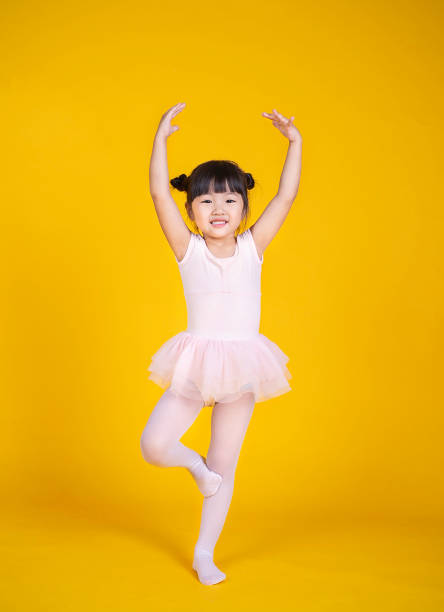 portrait of little asian child girl dreams of becoming ballerina in a pink tutu skirt isolated on yellow background. happy young girl practise her dance. education childhood toddler lifestyle concept - toddler music asian ethnicity child imagens e fotografias de stock