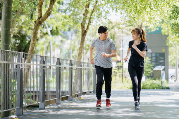 energica giovane coppia che fa jogging insieme al parco cittadino al mattino - running jogging asian ethnicity women foto e immagini stock