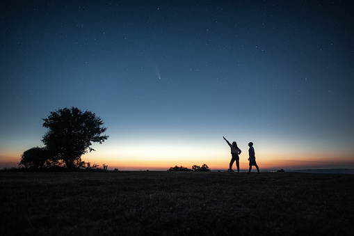 Silhouette of a young couple watching the Neowise comet  under the bright night sky after sunset