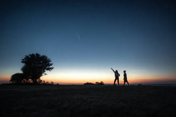 Photo of Young couple watching the Neowise comet under the bright night sky