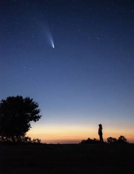 Silhouette of a young woman watching the Neowise comet  under the bright night sky after sunset
