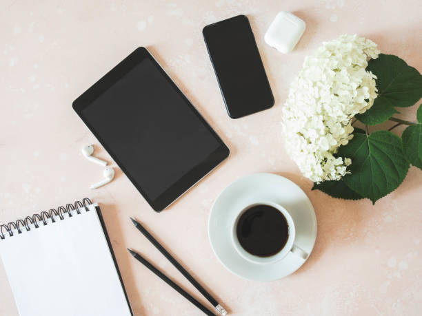 istock Home office desk workspace with black smartphone, black tablet, black coffee in cup, white hydrangea, white earphones and graphite pencils on pink background. 1257362547