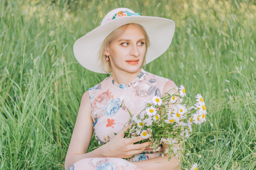 Pretty woman with bouquet of daisies on the high grass background in summertime season.