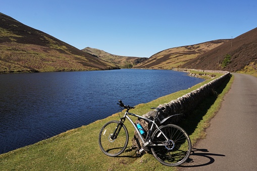 Pentland Hills, Scotland - 6 May 2020: A bicycle is resting against the wall that runs alongside Loganlea reservoir in the Pentland Hills. The access road running alongside the wall is closed to most traffic and is a popular route for pedestrians and cyclists.