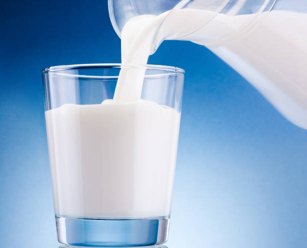 istock Milk poured from jug into glass on blue background 1257375529
