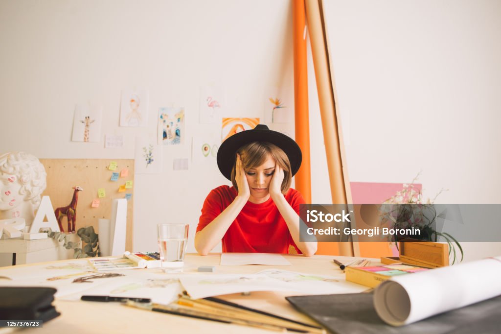 Sad girl Illustrator artist clutched head sitting at the table in studio. Photo for advertising art courses or blog Sad girl Illustrator artist clutched head sitting at the table in studio. Photo for advertising art courses or blog. High quality photo Animator Stock Photo