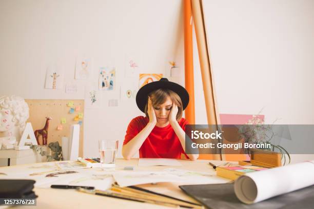 Sad Girl Illustrator Artist Clutched Head Sitting At The Table In Studio Photo For Advertising Art Courses Or Blog Stock Photo - Download Image Now