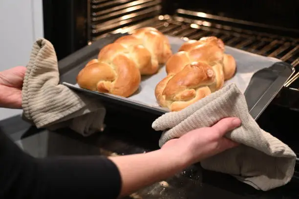 Jewish woman taking out baked Challah Bread out of the oven before Sabbath Jewish Holiday.