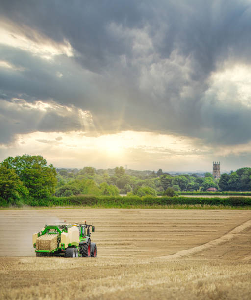 istock Straw or hay Baler machine pulled by a tractor, discharging a compacted straw bale from the rear in a field of recently harvested barley on the outskirts of Cirencester in the Cotswolds 1257384015