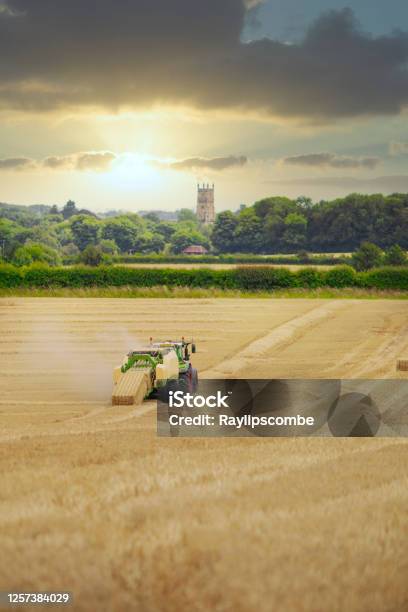 Straw Or Hay Baler Machine Pulled By A Tractor Discharging A Compacted Straw Bale From The Rear In A Field Of Recently Harvested Barley On The Outskirts Of Cirencester In The Cotswolds Stock Photo - Download Image Now