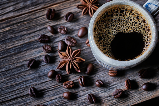 Hot Coffee Cup Concept. Pouring coffee into white coffee cup, mug with classic vintage grinder espresso manual and beans, natural steam smoke on old wood table in morning black backgrounds