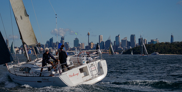 Sydney, NSW, Australia - June 14, 2020: Hubcap 2 and other yachts participating of a Sunday regatta in Sydney Harbor, out of Cruising Yacht Club of Australia. \nBoat sailing away with cityscape as backdrop. Series.