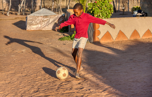 African child playing soccer on the dirt in his yard in a village in Botswana