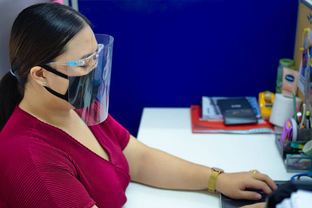 Woman wearing face mask while working in office A young, beautiful woman wearing a face mask as protection against covid-19 while working inside an office. office cubicle mask stock pictures, royalty-free photos & images