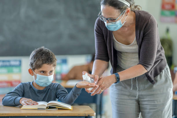 istock Masked teacher offering hand sanitizer to students in class 1257395081