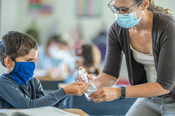 istock Masked teacher offering hand sanitizer to students in class 1257395119