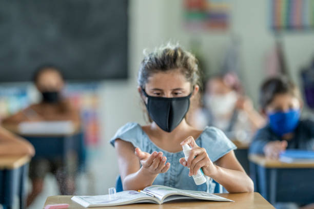 istock 12 year old student using a spray sanitizer in class while wearing a mask 1257395176
