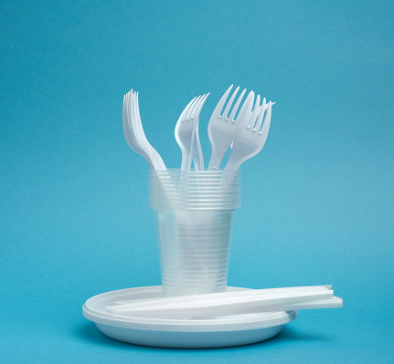 disposable plastic tableware plates, cups, forks and knives on a blue background, picnic set