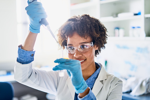 Smiling young female scientist using a pipette while working with research samples in a lab