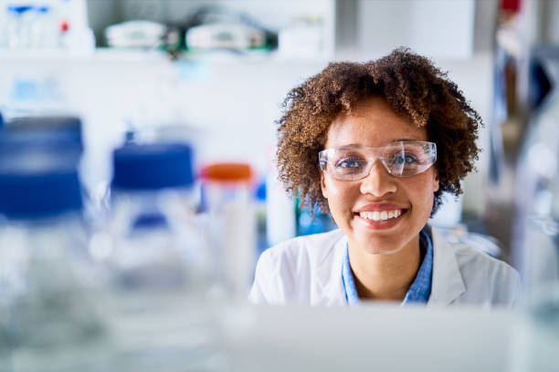 giovane scienziata sorridente in piedi accanto a scaffali in un laboratorio - research smiling scientist women foto e immagini stock