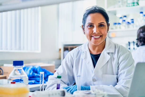 scienziata sorridente che lavora a un tavolo in laboratorio - research smiling scientist women foto e immagini stock