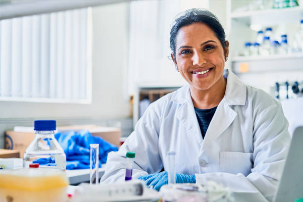 улыбающаяся женщина-ученый, исследующая за столом в лаборатории - happiness working people pathologist стоковые фото и изображения