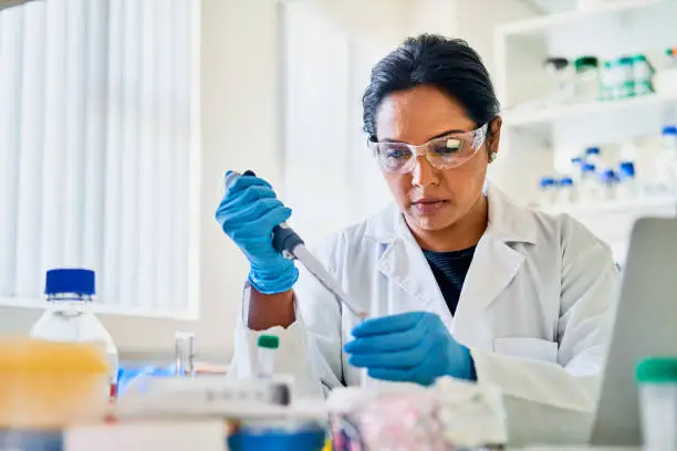 Female scientist using a pipette to extract research samples while working alone at a table in a lab