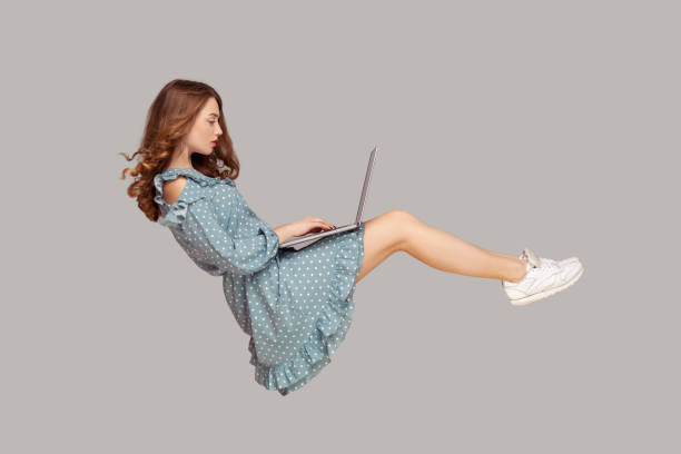 istock Hovering in air. Pretty girl ruffle dress levitating, typing keyboard using laptop for work online, surfing web social networks 1257417430