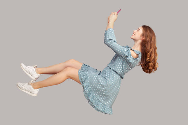 hovering in air. smiling girl ruffle dress levitating with mobile phone, reading message chatting happy joyful - levitation imagens e fotografias de stock