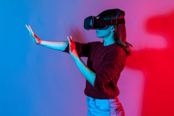 istock Side view, girl with virtual reality glasses on head playing game simulator, standing outstretched hands 1257417558