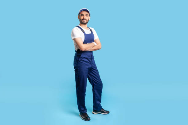 full length confident professional handyman in overalls standing with crossed hands, smiling at camera - men mechanic manual worker craftsperson imagens e fotografias de stock