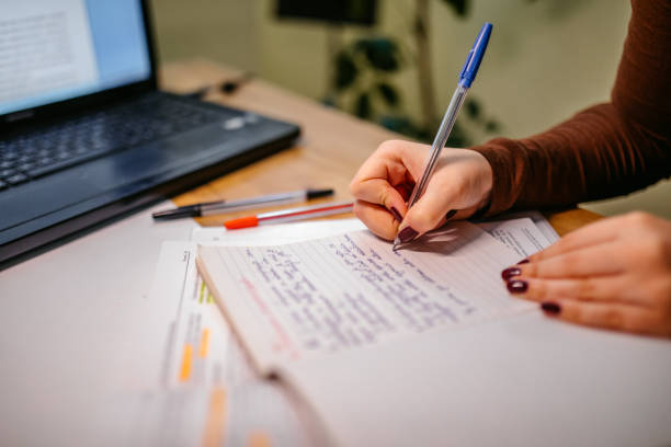 Close up of student woman hand studying and writing on agenda on a desk at home.
