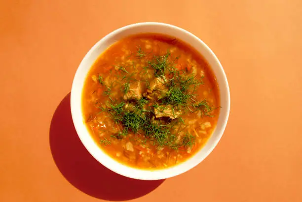 Photo of Kharcho soup in a white bowl on a bright orange background. Top view