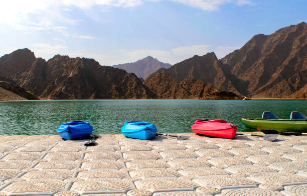Beautiful deep green Hatta lake between Hajar Mountains with many colorful kayaks parked on a pier stock photo