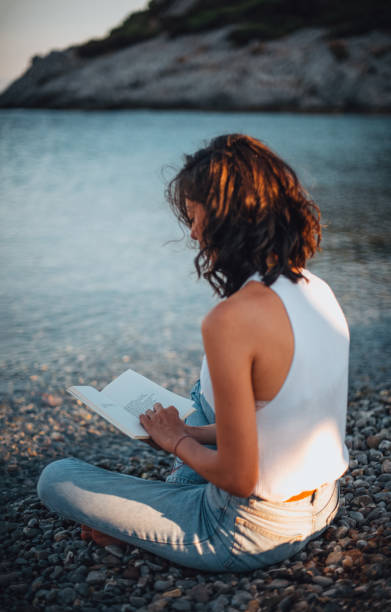 istock Young Woman Reading Analog Book at the Beach 1257428332
