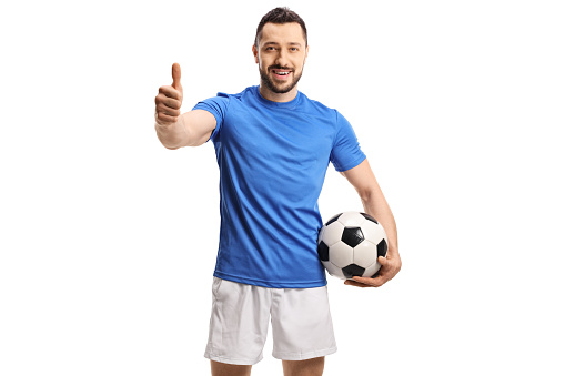 Soccer player holding a ball and giving a thumb up isolated on white background