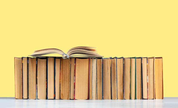 istock Open hardback book, diary, fanned pages on stack of books on white table in library. Books stacking. Back to school concept. Copy Space. Education learning background 1257437402