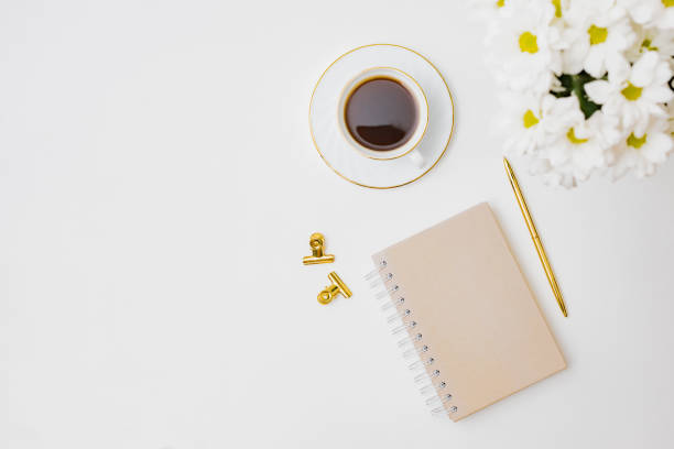 Flat lay blogger or freelancer workspace with a notebook, white flowers, a cup of coffee on a white background