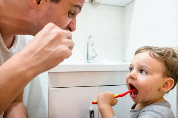 Father and toddler son brushing teeth in the bathroom