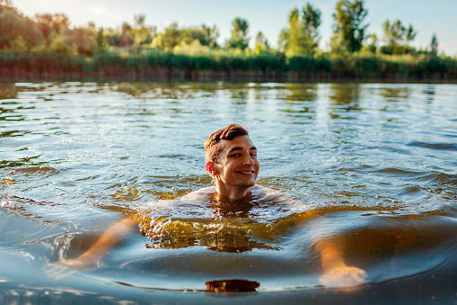 Young handsome man swimming in river. Happy guy smiling in water. Summer vacation activities